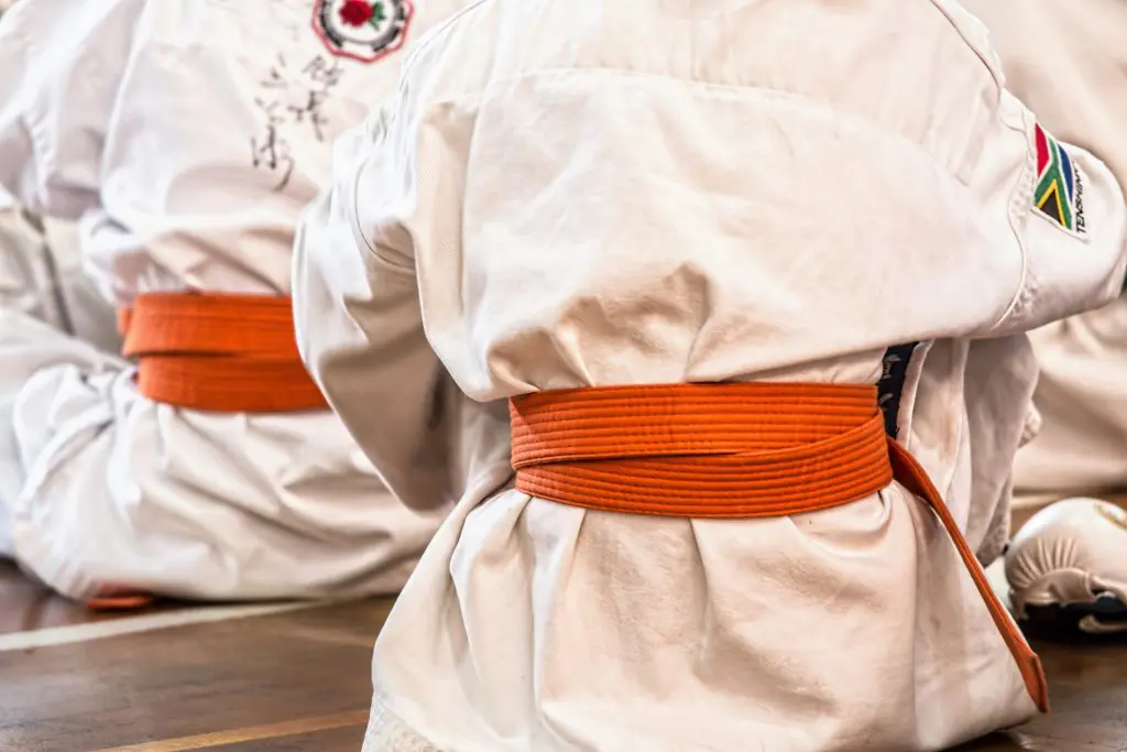 people wearing martial arts outfits and orange belts sitting on the floor